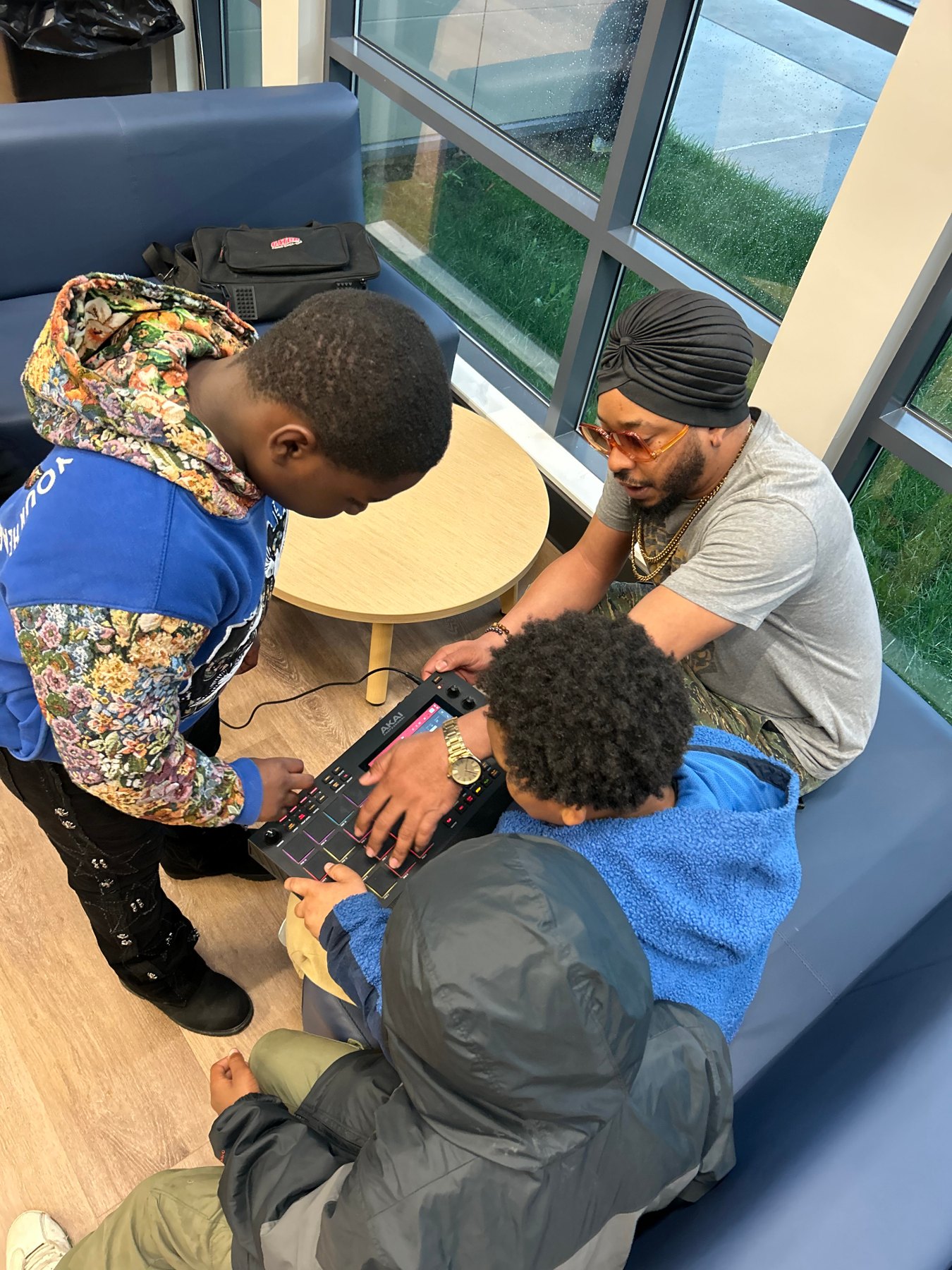 Older youth learning to make beats on an AKAI MPC with a mentor in a turban guiding their hands
