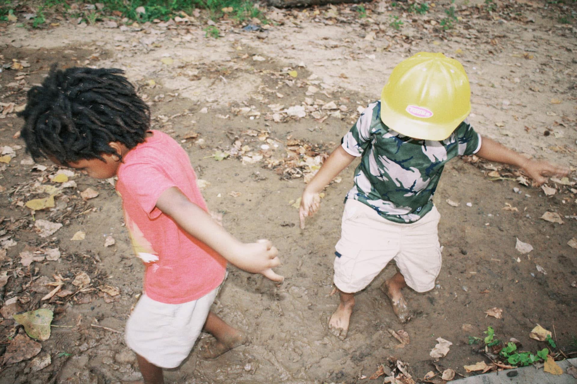 Two barefoot kids exploring a muddy patch together
