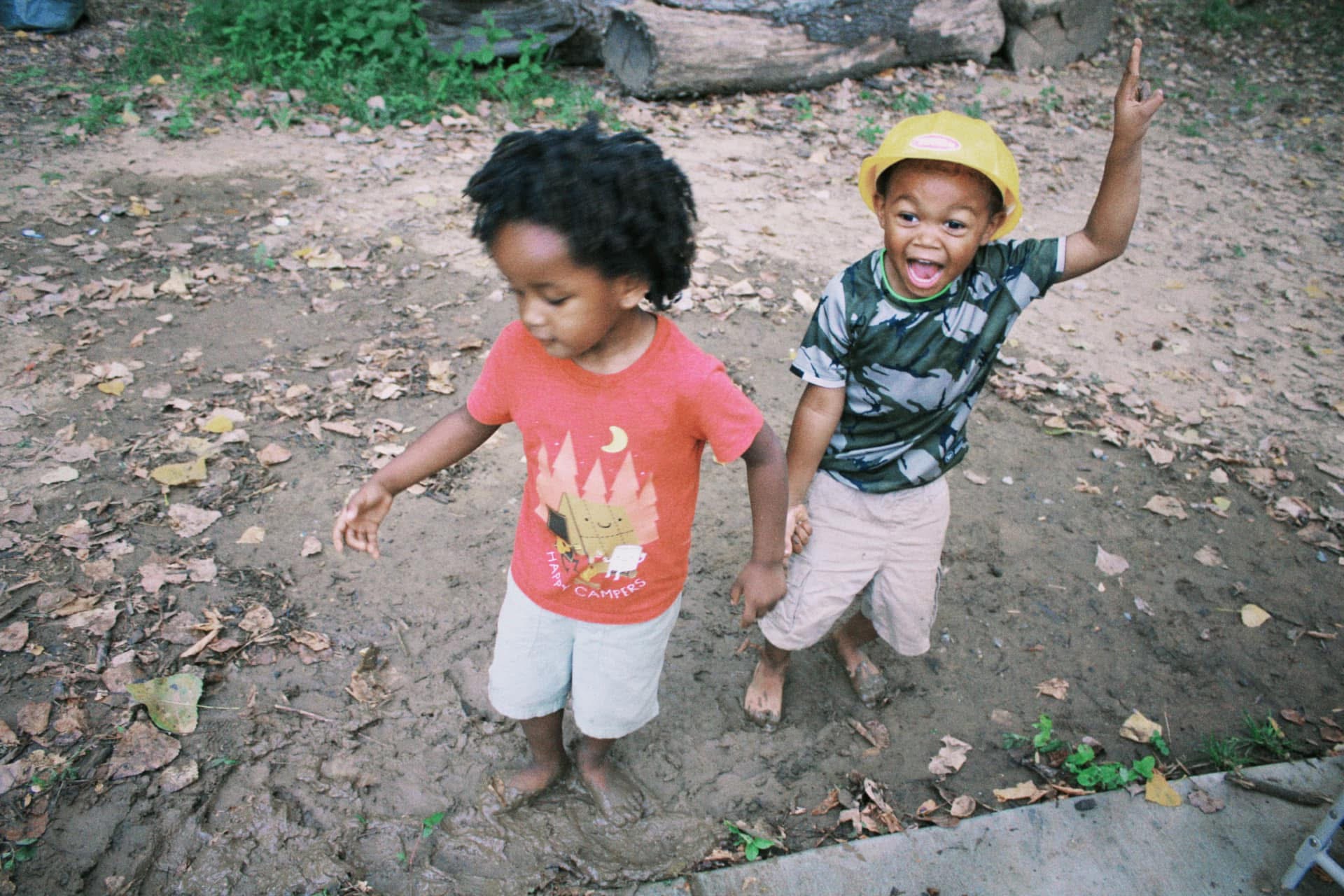 Two cousins jumping in the mud, one cheering with arms raised