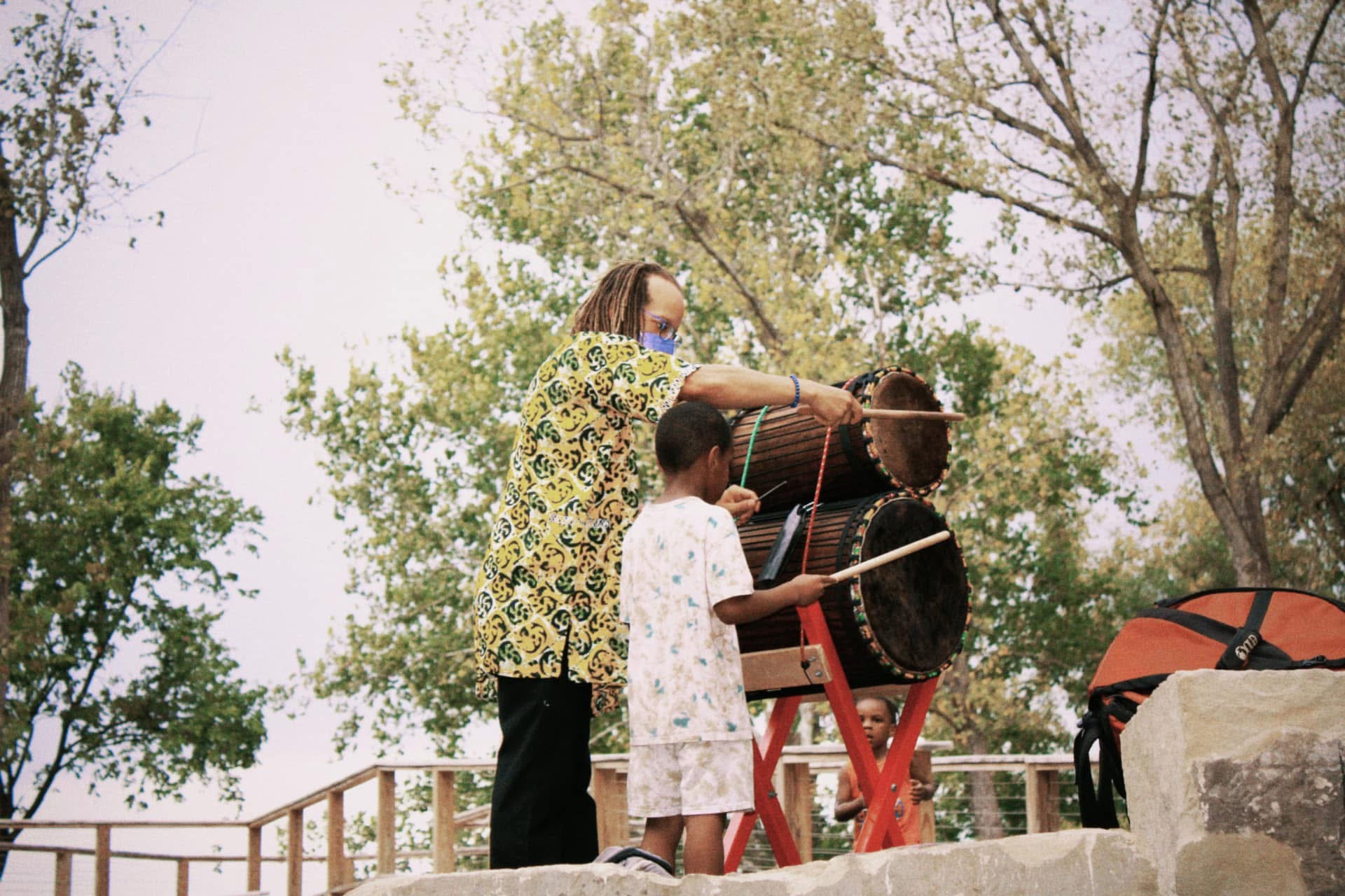 An elder teaching a child to play traditional drums above the river