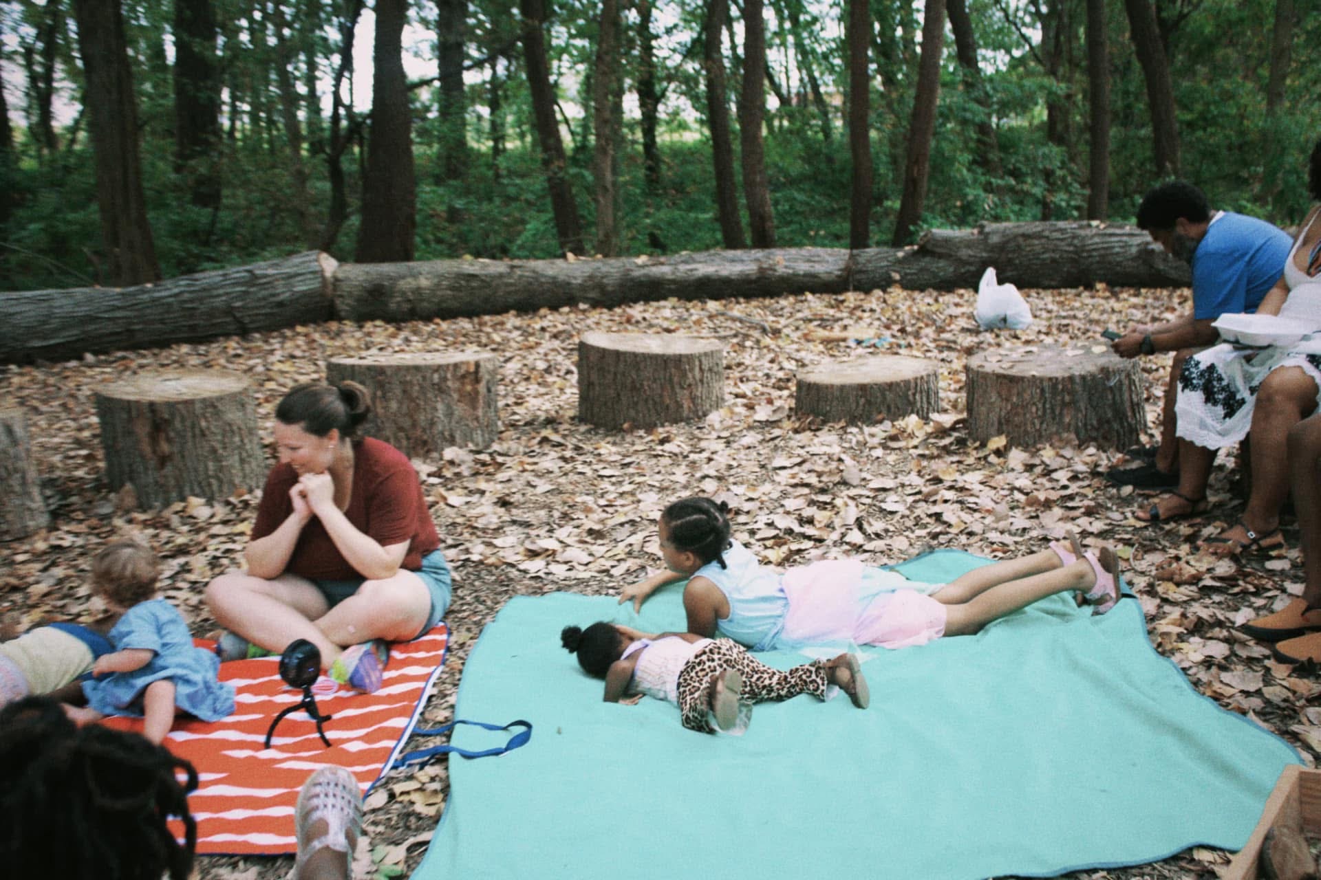 Children resting together on blankets inside a circle of cut tree stumps