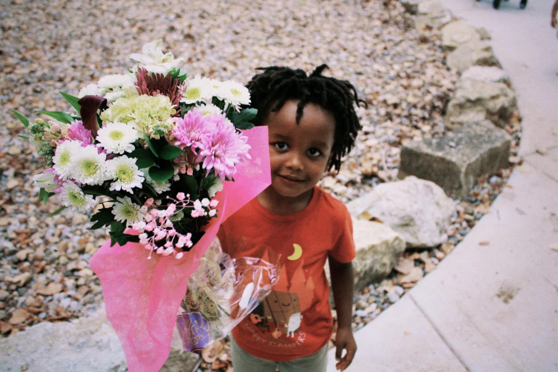 A young boy beaming as he holds a bright bouquet of flowers