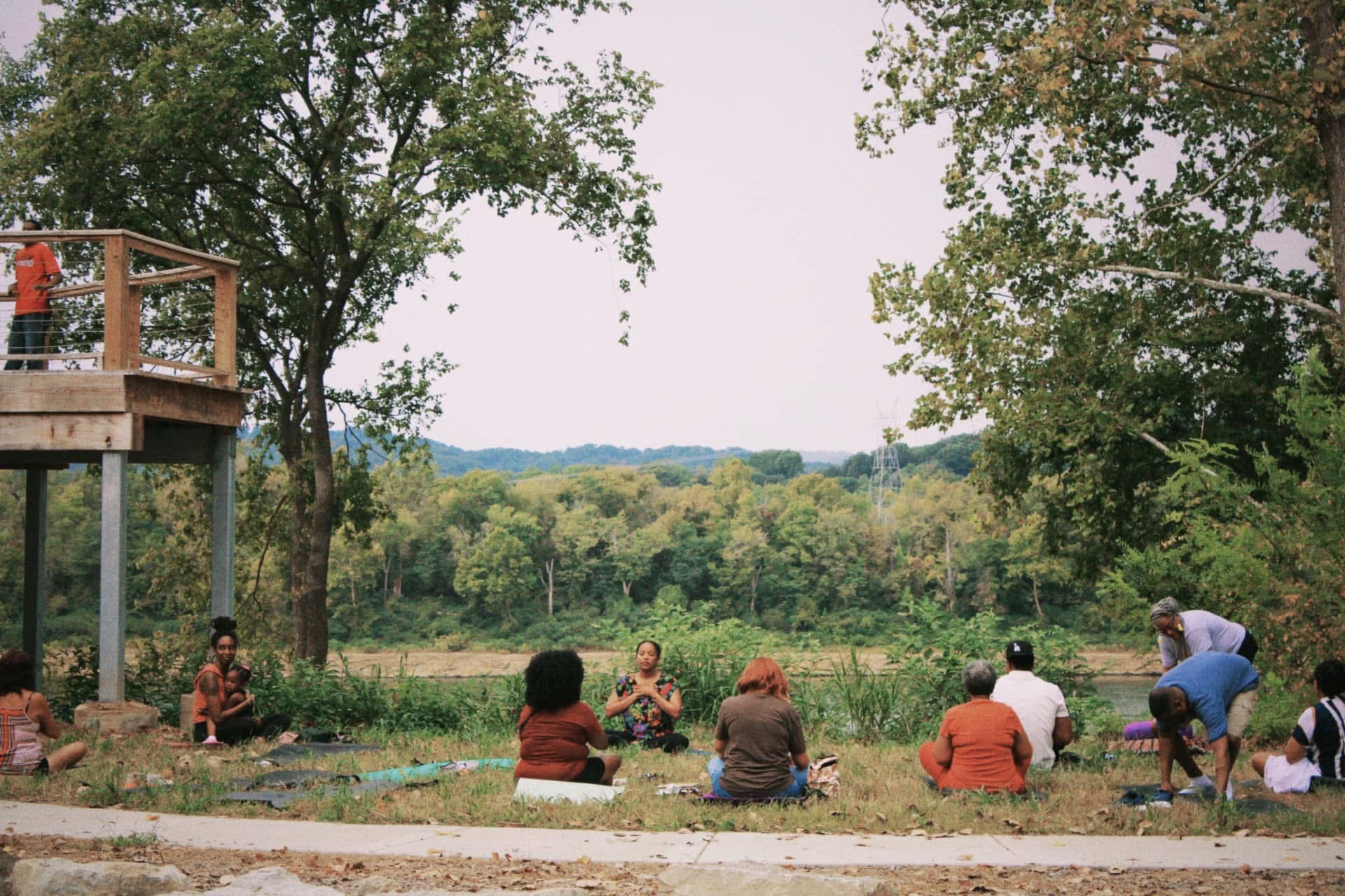 A yoga circle gathered along the riverbank with a child held in arms