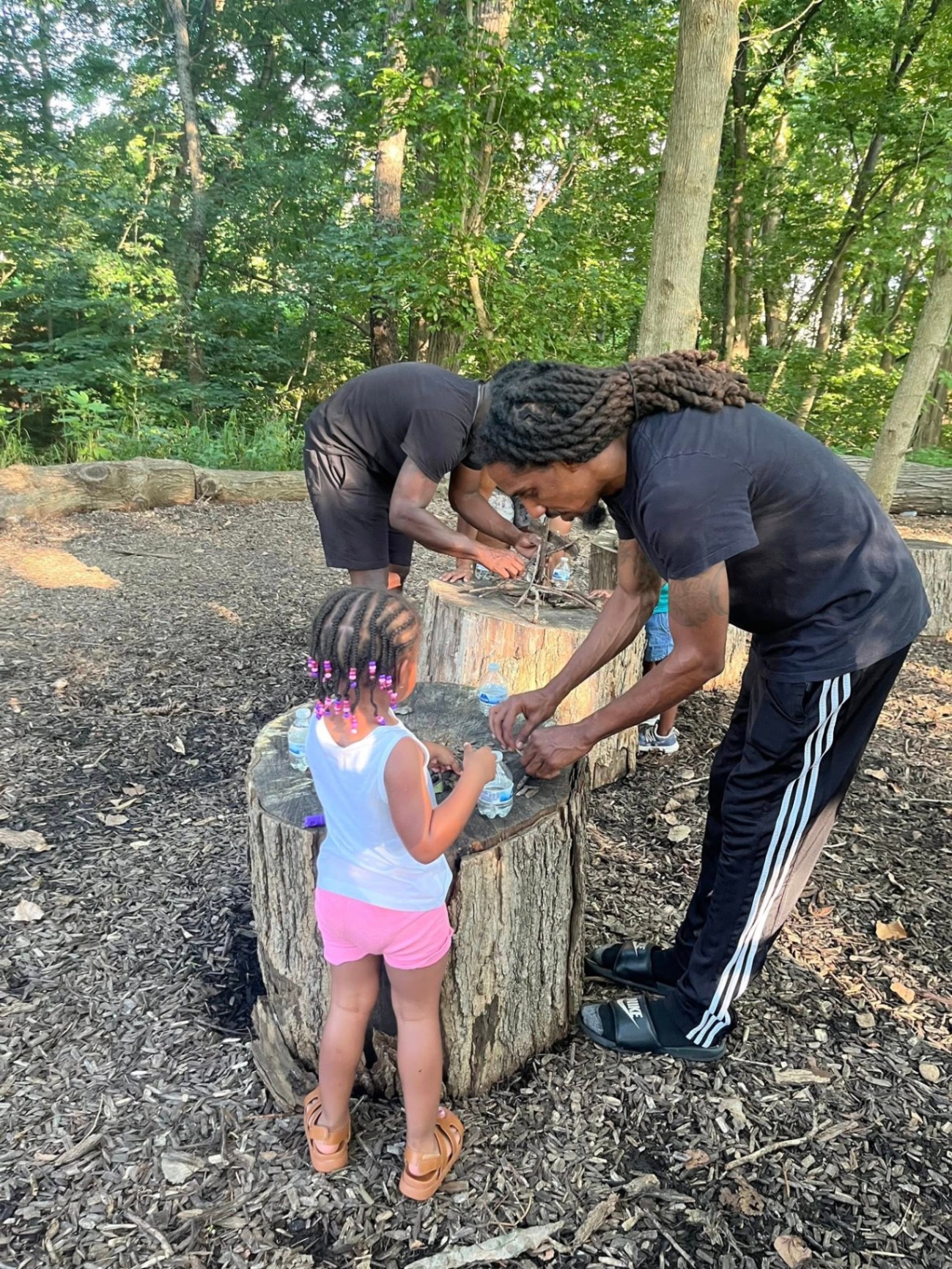 A father and young girl building together on a wood stump in the forest
